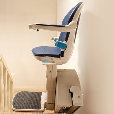 A stair lift sits against a wall, appearing ready for use, within a home setting.