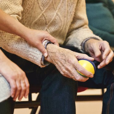 Older man sat down holding a ball as a women rests her hand on his arm