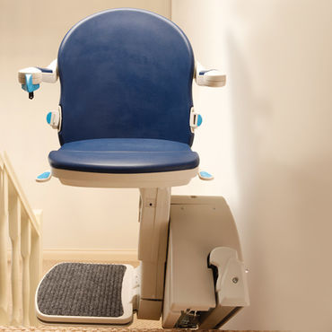 A stair lift chair sits against a wall, appearing to be stationary, in what seems to be a residential hallway.