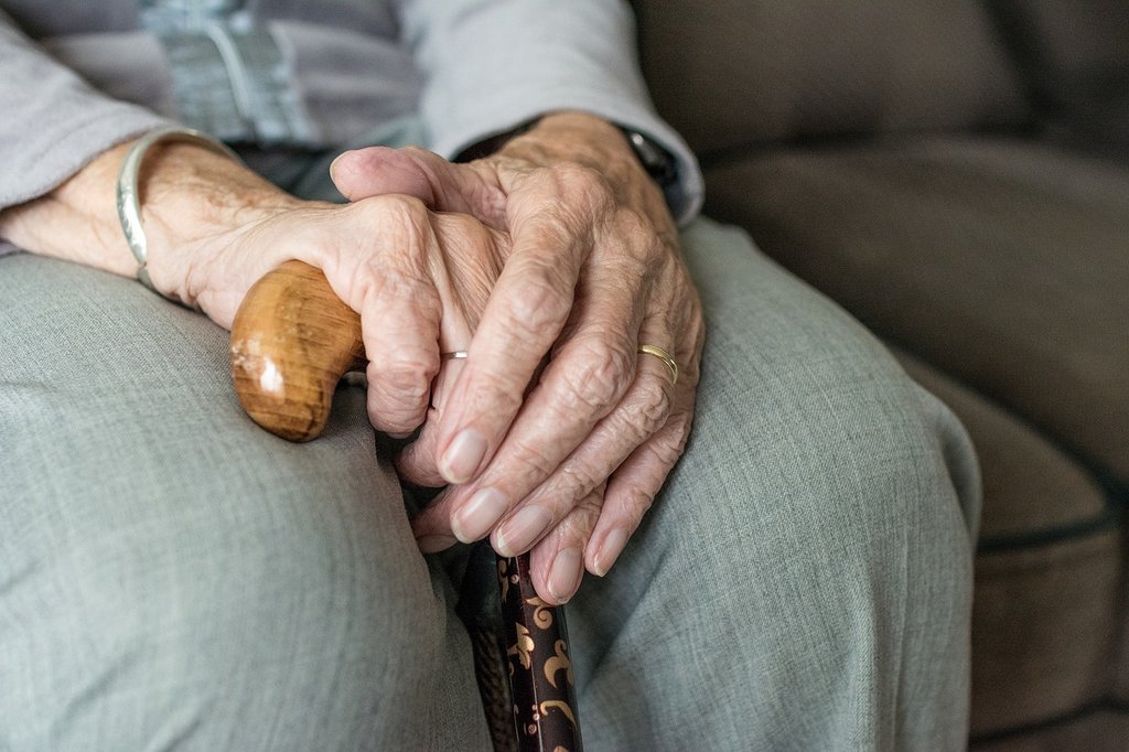 old person sitting down holding walking stick