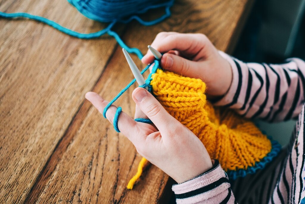 A lady knitting with yellow and blue yarn