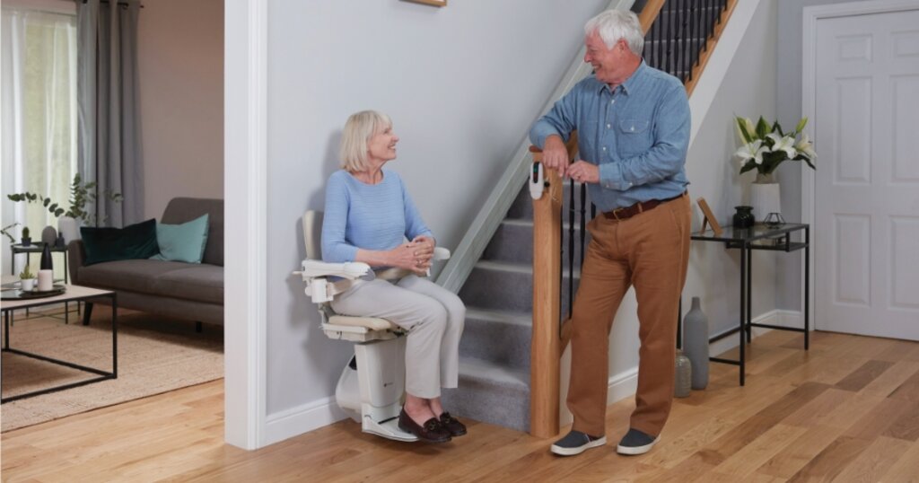 A woman riding a stairlift while talking to a man