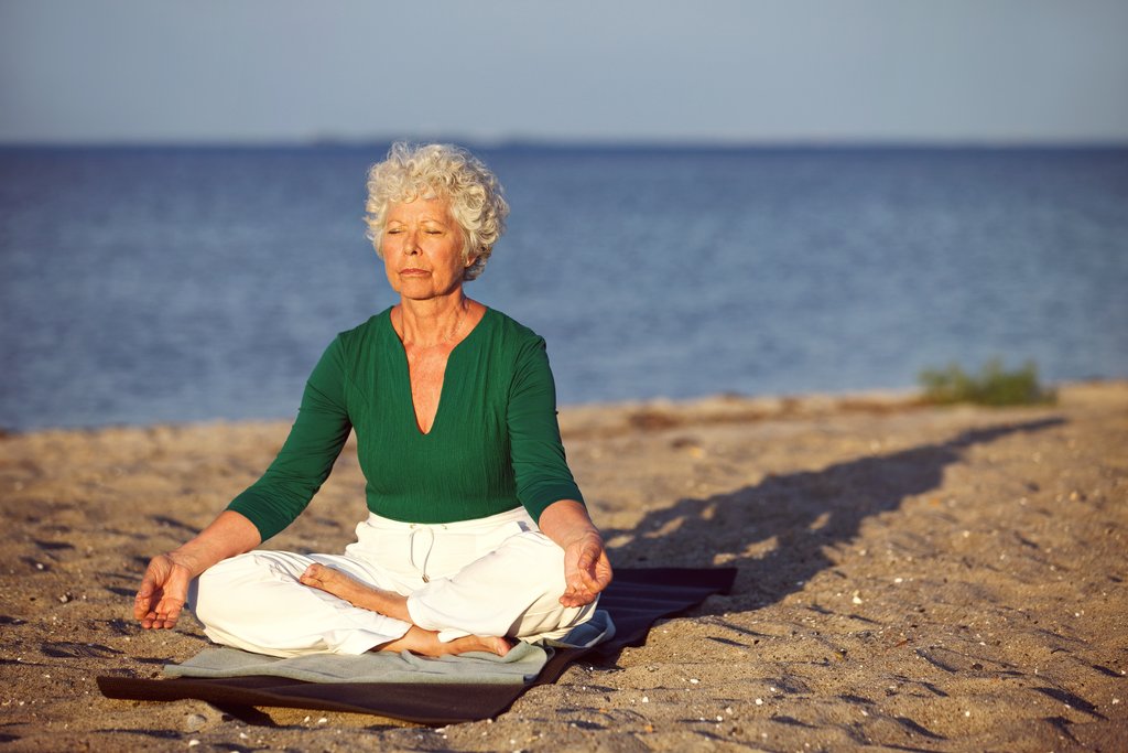 An older lady doing yoga on the beach